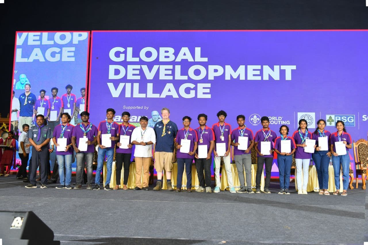 The Sairam team on stage with our certificates, Global Development Village screen behind us