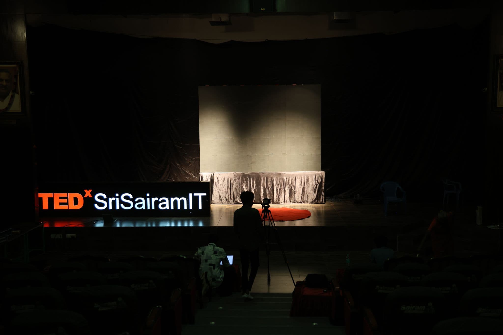 The TEDx sign lit up next to an empty stage during setup, camera on a tripod ready to go