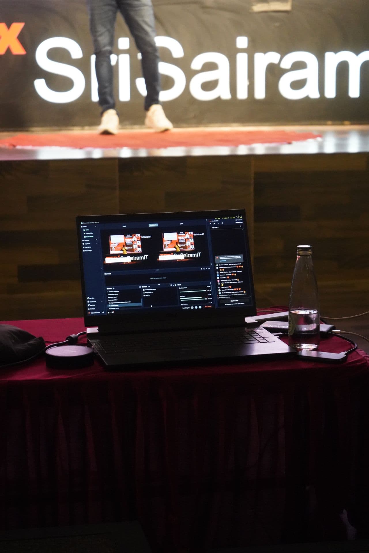 The laptop running the livestream from the tech desk, stage in the background